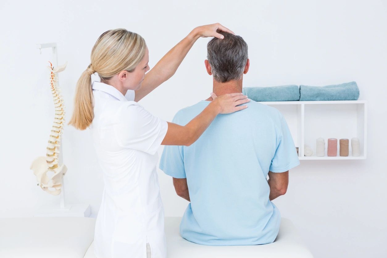 female chiropractor doctor assessing a chiropractic patient's neck in an office with a model spine in the background